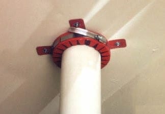 A red intumescent fire collar fitted around a plastic soil pipe where it passes through a fire-rated wall or floor